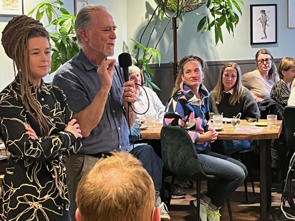 Foto från medlemsfika där Amanda Lind och Daniel Helldén svarar på frågor. Amanda och Daniel står brdvid varandra och Daniel håller i en mikrofon.