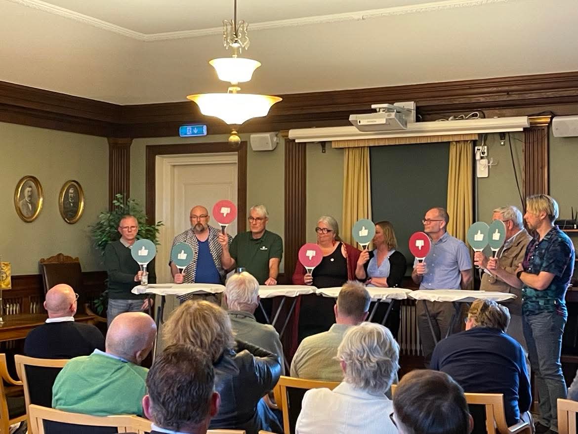 Paneldebatt "Grilla en politiker". Företrädare för de olika partierna står på rad och håller i skyltar i händerna som är gröna med tummen upp eller röda med tummen ner.