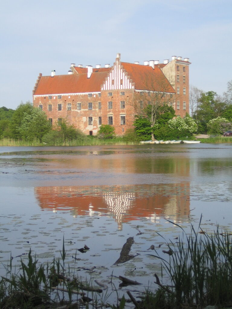 Svaneholms slott speglar sig i sjön framför.