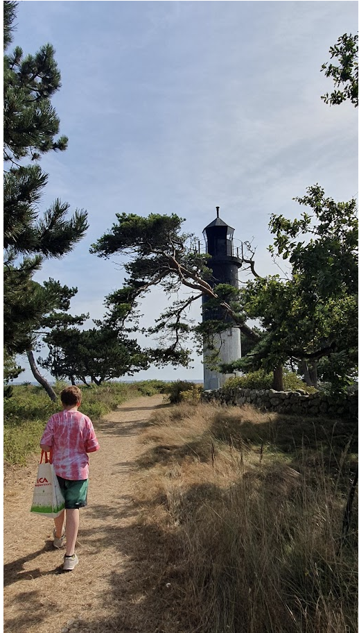 Ett barn går på stranden mot en fyr