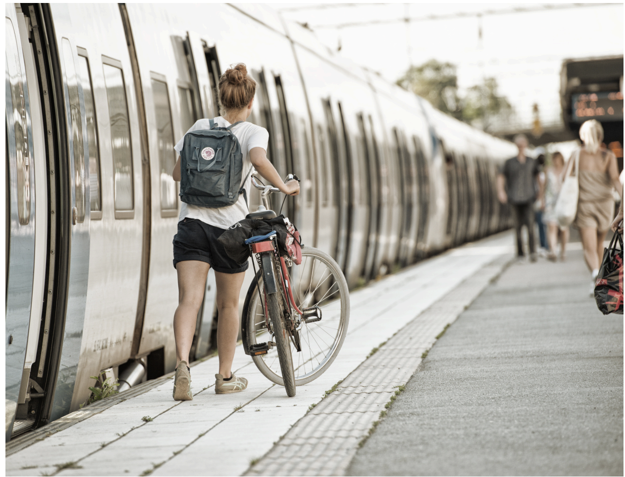 En person står på perrongen med sin cykel, klar att gå på tåget.