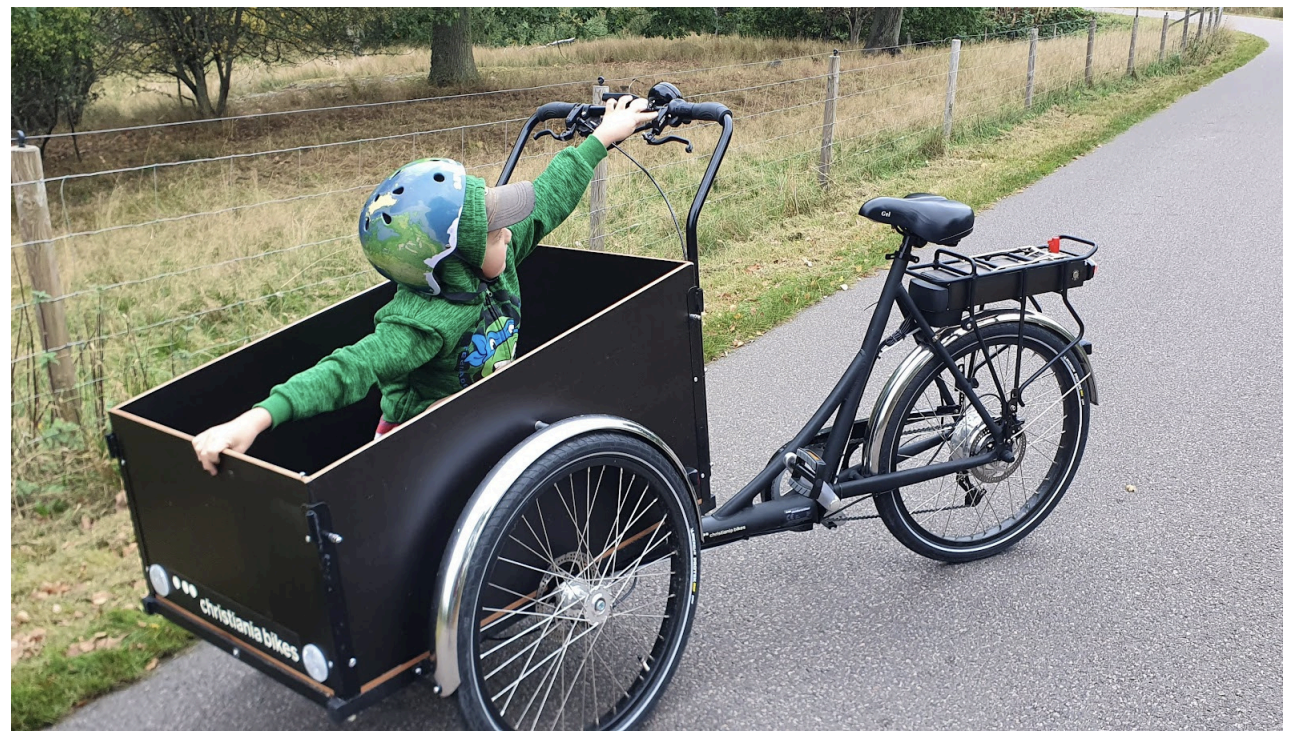 Ett barn sitter i en lådcykel med hjälm på huvudet och väntar på att få åka vidare