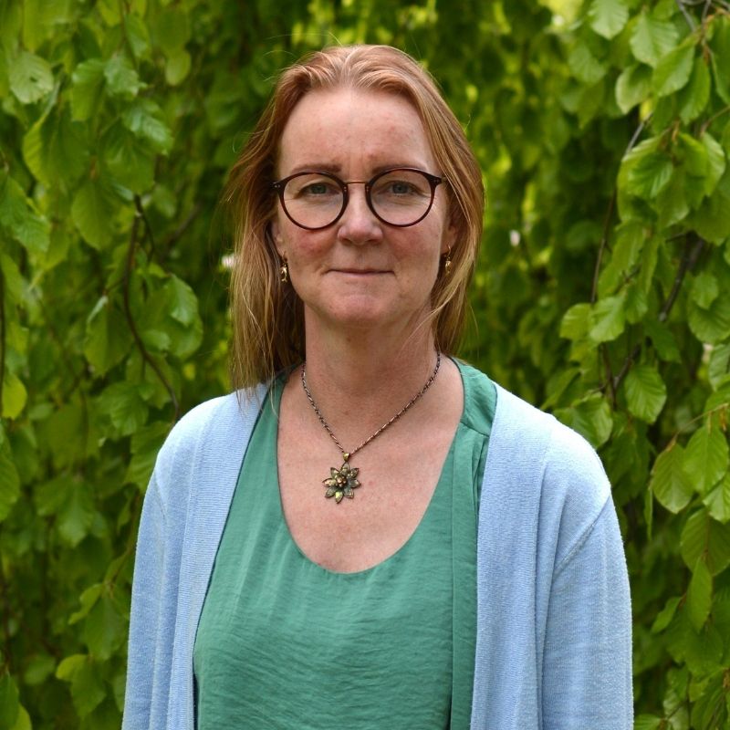 Porträtt av Pernilla Sporre utomhus framför gröna löv.