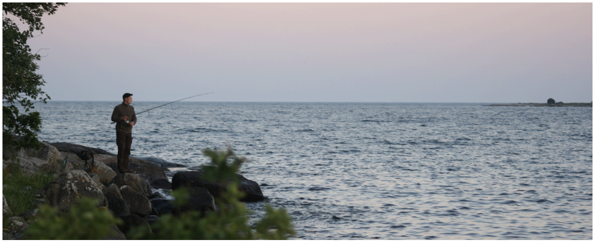 En person står på en sten vid havet och fiskar